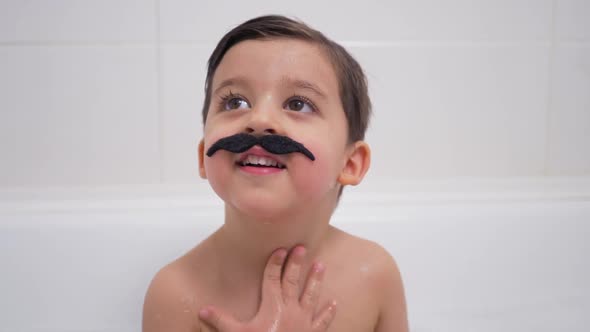 Small Boy with a Black Mustache Sits in the Bathroom