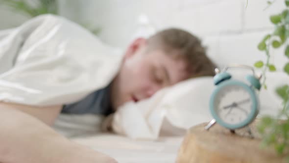 Man Sleeps in Bed with Clock in Foreground