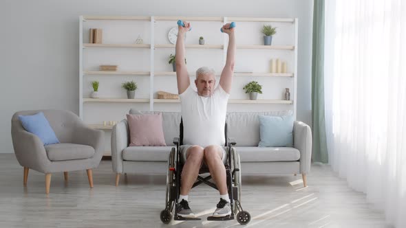 Impaired Man Exercising With Dumbbells Sitting In Wheelchair At Home