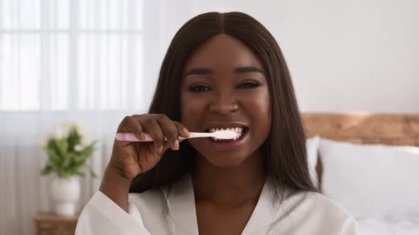 Black Woman Cleaning Teeth With Toothbrush Standing In Bedroom