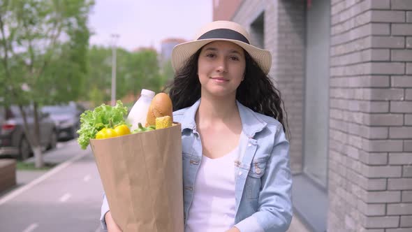 Young Beautiful Woman in a Denim Jacket and Hat Carries a Package with Products Having a Good Mood