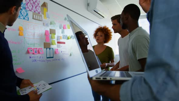 Team of executives discussing over sticky notes on whiteboard