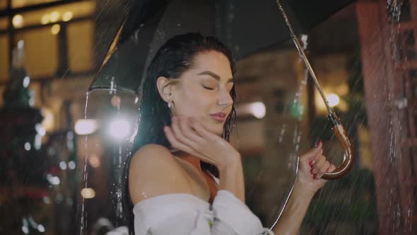 Passionate Wet Brunette Lightly Poses at Camera Under Night Rainfall