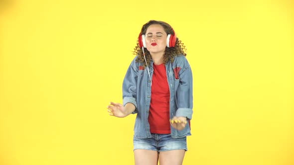 Cheerful Girl Dancing in Big Red Headphones on Yellow Background at Studio