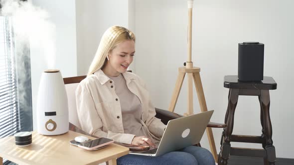 Pretty Blonde Woman Working on Laptop Near Air Purifier and Moisturizer Appliance