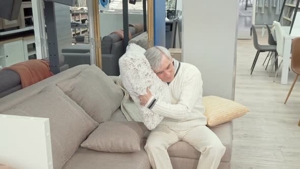 Cheerful Elderly Man Trying Soft Cushions on Sale at Furniture Store