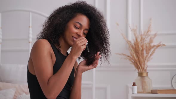 Black Woman Applies Cosmetic Oil From a Bottle with Dropper on Her Afro Hair