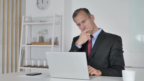 Pensive Middle Aged Businessman Thinking and Working on Laptop