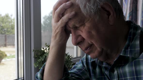 Elder Man Looks Out Of Window Lowers Head On Arm Headache High Blood Pressure