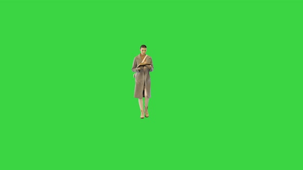 Young Woman in Stylish Clothes Walks with a Book Stops and Closes It on a Green Screen Chroma Key