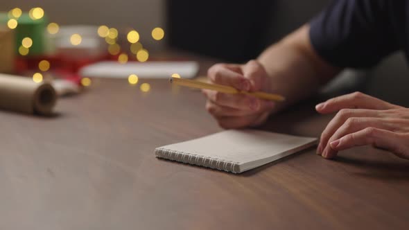 Orbit Shot Man Tapping His Finger Thinking About Christmas Gifts Notepad Pencil Under Warm Light