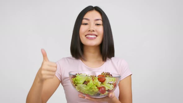 Cheerful Japanese Lady Holding Salad Bowl Gesturing ThumbsUp White Background