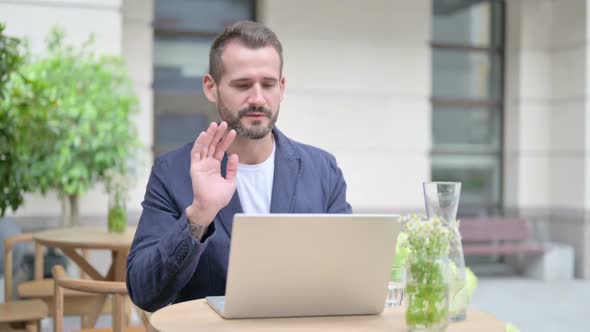 Man Talking on Video Call on Laptop Sitting in Outdoor Cafe