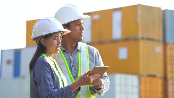 Two logistic staff discussing while checking and control loading containers box from cargo.