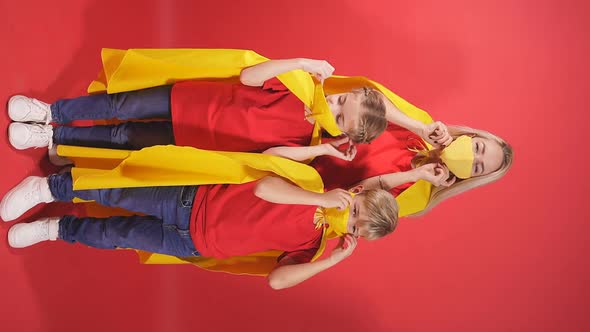 Blonde Caucasian Mother Stand with Son and Daughter in Superhero Cloaks and Medical Masks