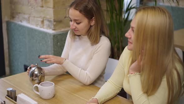 Slim Young Woman Pouring Aromatic Tea From Teapot in Cup in Slow Motion Smelling Hot Drink Smiling