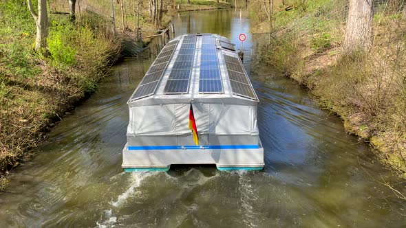 Tilt up shot of electric boat with solar panels cruising on rural river in nature during sunlight. G