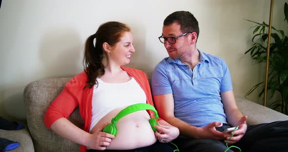 Pregnant woman placing headphones while interacting with man