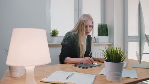 Business Women Working on Tablet in Office. Attractive Blond Female with Long Hair in Elegant Suit