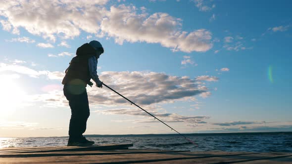 A Boy Sits Down Onto a Quay While Fishing