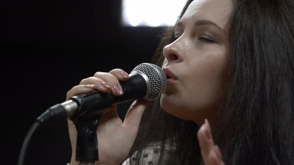Young brunette woman with microphone is emotionally singing song in professional recording studio.