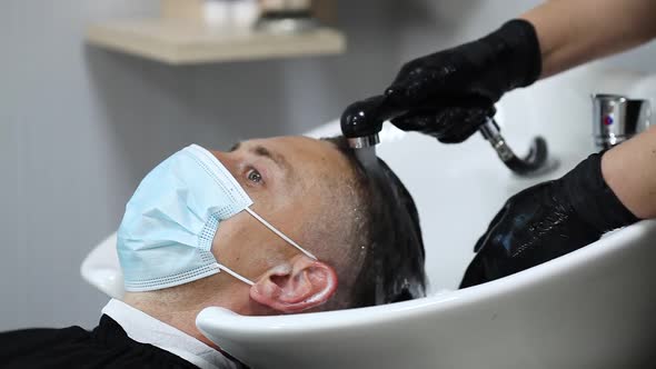 Female hairdresser hands in rubber gloves washes the head of a medical mask man. A hairdresser with