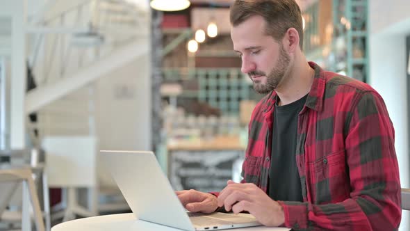 Serious Young Man with Laptop Pointing at the Camera 