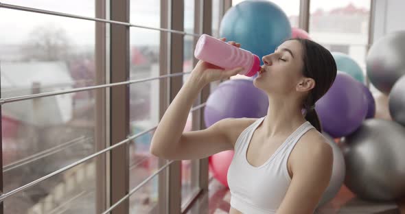 Tired Woman Drinks Water After Fitness Workout in the Gym