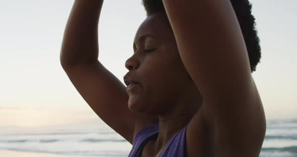 African american woman practicing yoga and meditating on sunny beach