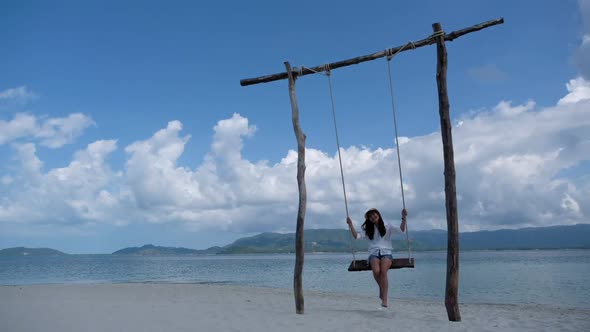Slow motion of a beautiful young asian woman sitting on wooden swing in the sea