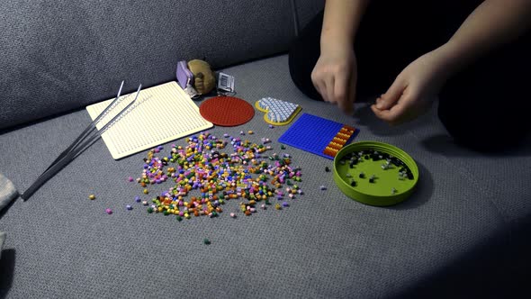 Child making art with perler beads,on the sofa.