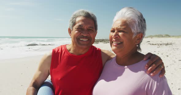 Portrait of hispanic senior couple standing on beach, holding yoga mat and smiling