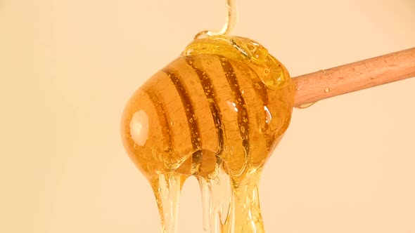 Close up honey flowing from wooden dipper on beige