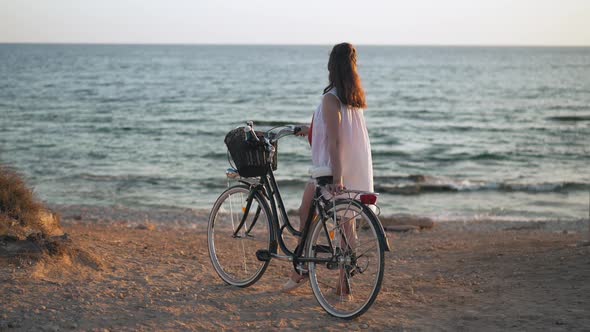 Young Carefree Happy Woman with Bicycle Looking Away Smiling Standing on Yellow Beach at