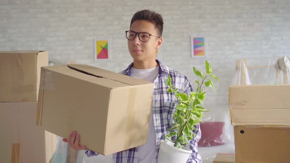 Positive Young Sian Man with a Flower and a Box in His Hand Moves To a New Apartment