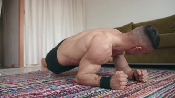 A Young Bodybuilder Training in His Room on a Mat and Makes an Original Plank Pumping the Muscles of