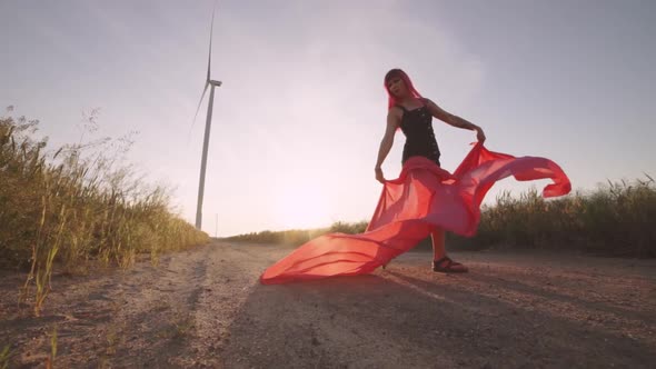 Woman with Pieces of Red Cloth Dance Near the Field with Wind Generators 
