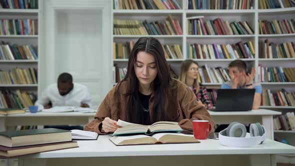 Young Woman with Long Hair Reading Book in Library and Looking at Camera with Lucky Smily