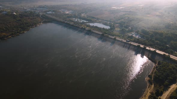 the Flight of the Drone Over a Highway with Moving Cars and a Lake in the Suburbs