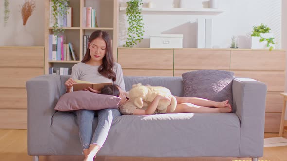 Mom is reading for her child and her child is lay down on her lap while she has been sitting on the