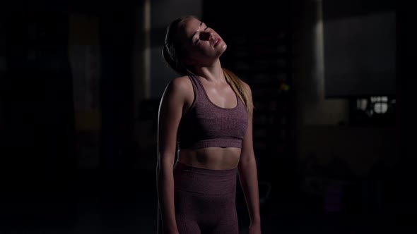 Young Sportswoman Warming Up Neck Muscles Stretching in Slow Motion Standing in Darkness