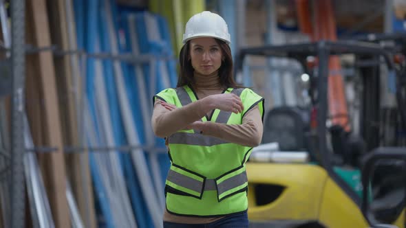 Front View Portrait of Confident Serious Caucasian Woman in Hard Hat and Vest Crossing Hands Looking