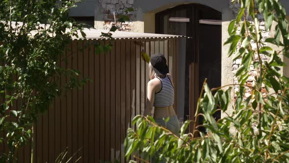 girl in a cap paints a garage with a roller outside