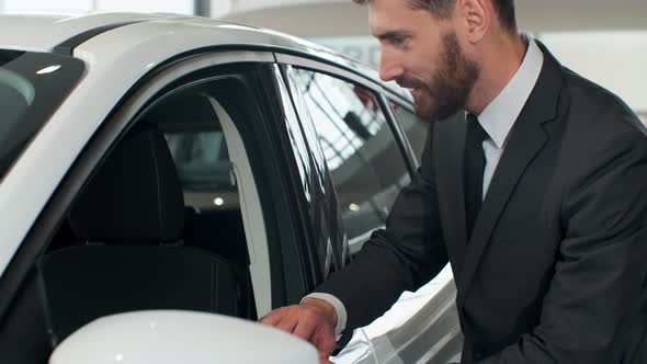 Stylish Man Is Choosing New Automobile Walking Around Luxury Car and Touching It in Car Dealership