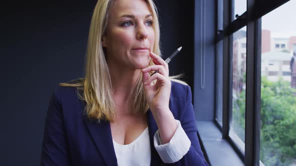 Caucasian businesswoman standing looking through a window in modern office