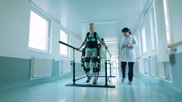 Doctor is Watching a Female Patient Using Exoskeleton for Walking