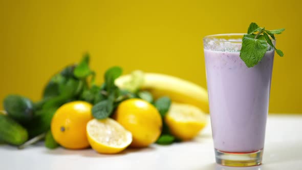 Closeup Purple Milkshake with Berries and Mint Falling on Citrus Fruits at Background in Slow Motion