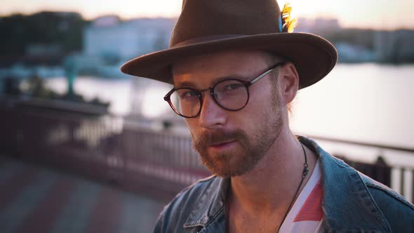 Colorful Portrait of Young Stylish Guy with Red Beard in Glasses and in Hat Looking at Camera During