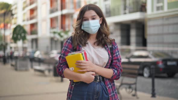 Portrait of Smart Charming College Student in Coronavirus Face Mask Posing on City Street with Books