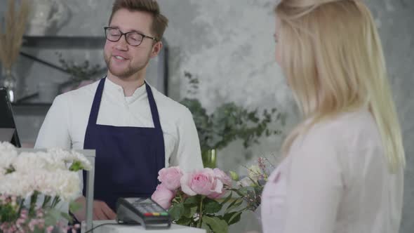 Attractive Young Male Sellers Working in Flower Shop at Checkout, Make Contactless Payments Through